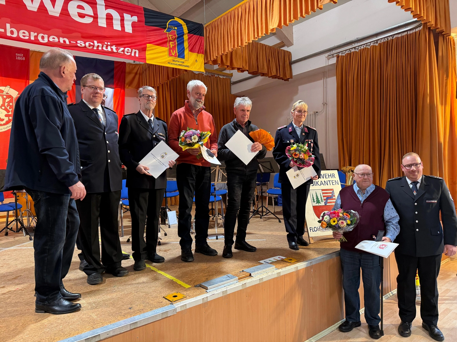 Kreisfeuerwehrverband Schmalkalden-Meiningen e.V. - Koordiniert die Aktivitäten und Veranstaltungen der Feuerwehr - Eine Gruppe von Menschen steht während einer Preisverleihung auf einer Bühne und hält Urkunden und Blumensträuße in den Händen.